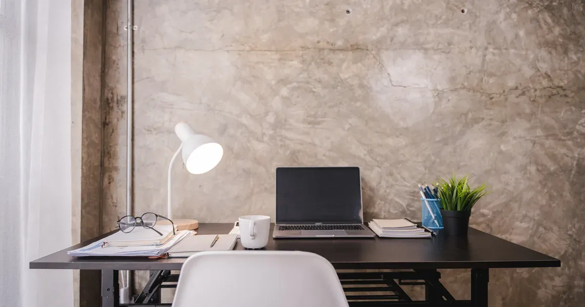 A tidy corner home office with a wooden desk, monitor at eye level, a small plant, and organized cables — natural light from a side window.