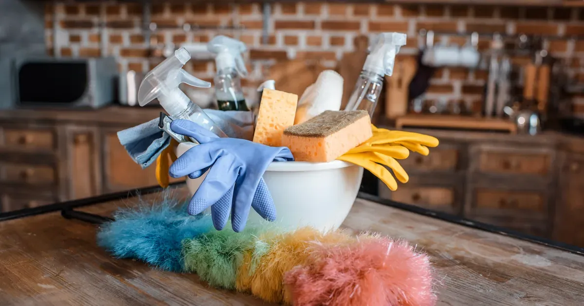 A clean, open front-load washing machine drum with a bottle of white vinegar and box of baking soda on a bright laundry room shelf nearby. Natural light, fresh and clean aesthetic.