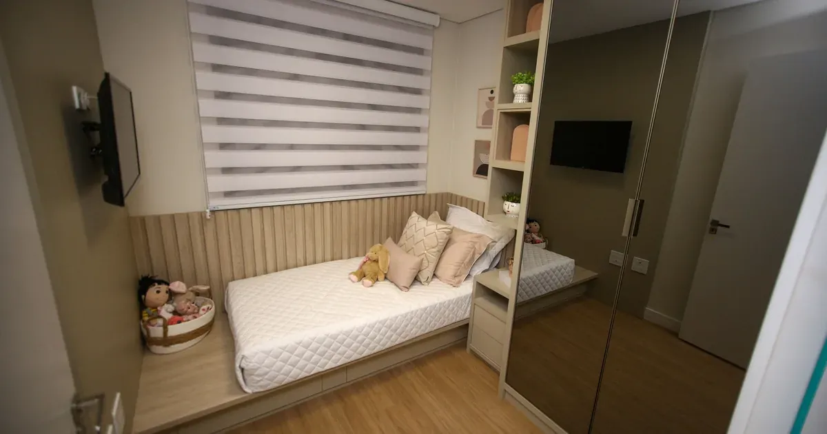 A bright, tidy small bedroom with floating nightstand shelves, under-bed storage bins, and floor-to-ceiling wall shelves. Natural light, neutral tones, real home setting.