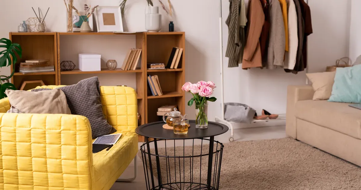 A bright, tidy small bedroom with floating nightstand shelves, under-bed storage bins, and floor-to-ceiling wall shelves. Natural light, neutral tones, real home setting.