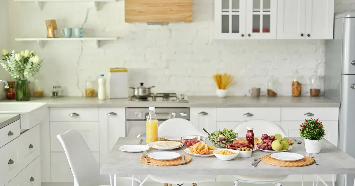 A compact white kitchen with a floating shelf above the counter, mugs hanging from hooks, and a rolling cart tucked against the wall — showing smart vertical storage in action.