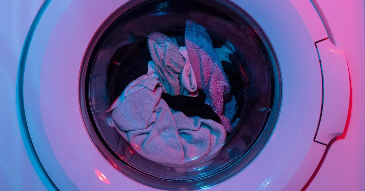 Close-up of a front-load washer drum with a clean rubber door gasket and sparkling interior, microfiber cloth and white vinegar bottle visible on top of the machine.