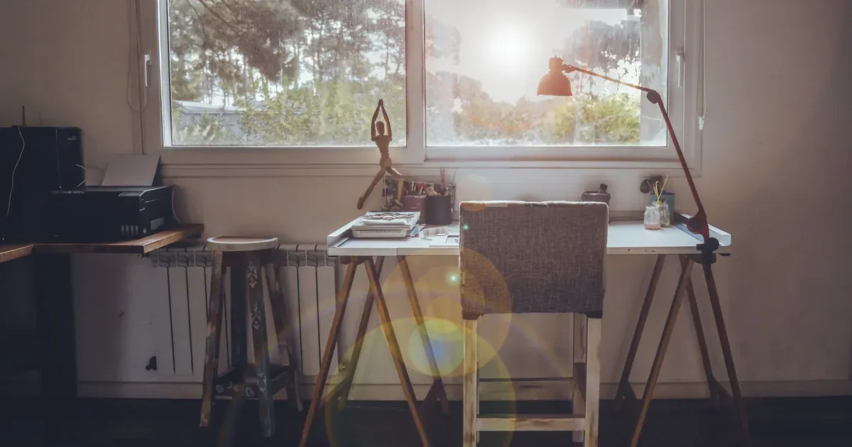 A calm, organized home office corner with a desk facing a window, clear surfaces, and contained cords.