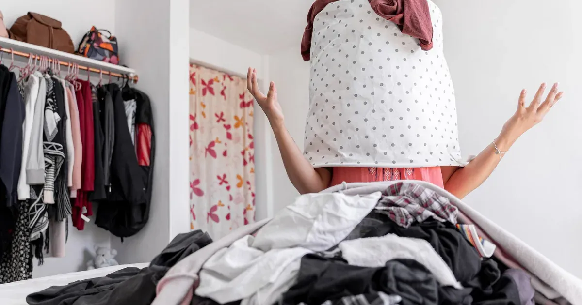 A half-cleared bedroom mid-declutter: one nightstand empty and wiped down, a sorting pile with donate box and trash bag visible nearby.
