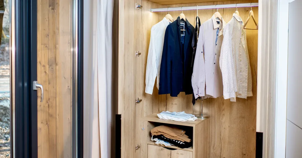 A small reach-in closet with a double hanging rod, slim matching hangers, and an over-the-door organizer, showing organized clothes with visible open space.