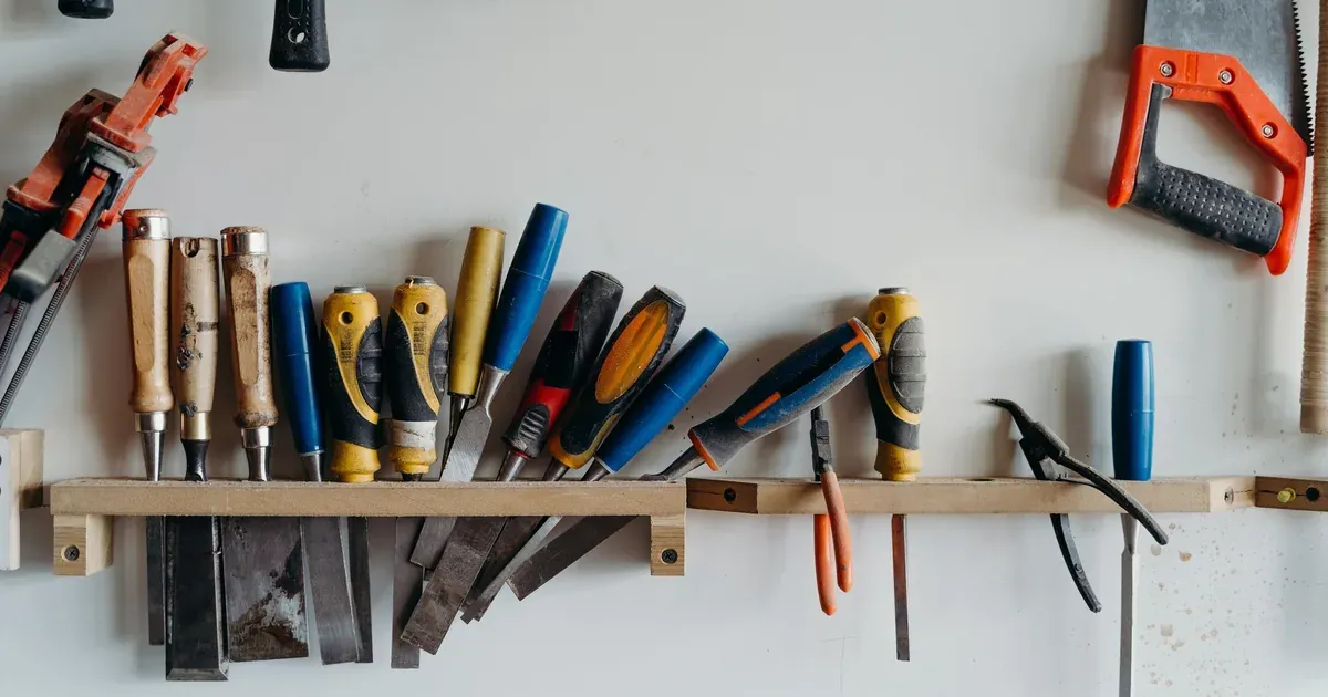 A garage wall fitted with slatwall panels holding hooks, baskets, and hand tools above a clean workbench.