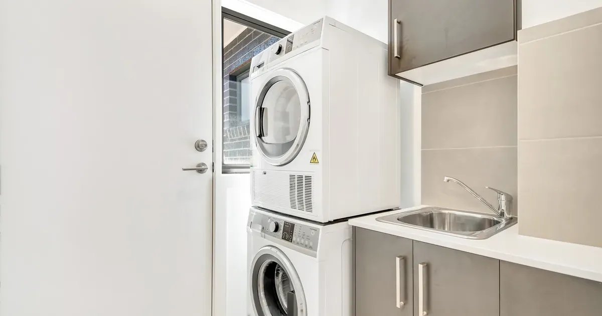 A narrow laundry closet with a wall-mounted drying rack, floating shelves above the machines, and a door-back organizer — showing vertical storage in a tight space.